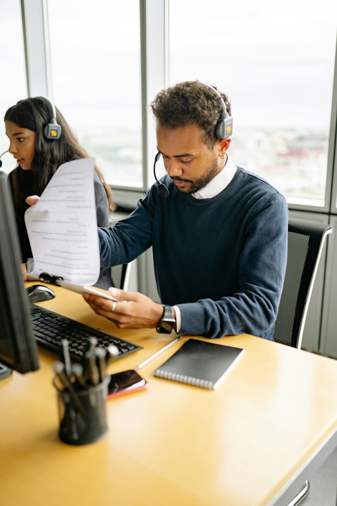 Two call center agents working together with documents and headsets in a modern office.